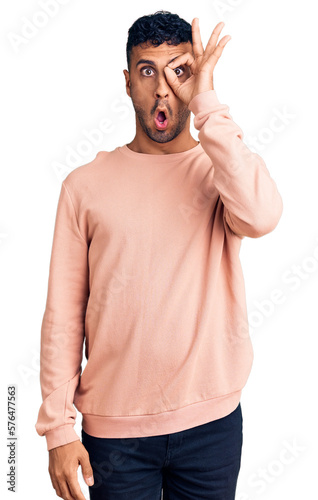 Young hispanic man wearing casual clothes doing ok gesture shocked with surprised face, eye looking through fingers. unbelieving expression.