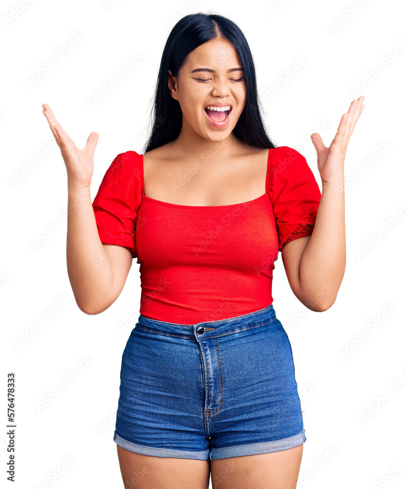 Young beautiful asian girl wearing casual clothes celebrating mad and crazy for success with arms raised and closed eyes screaming excited. winner concept Young beautiful asian girl wearing casual clothes celebrating mad and crazy for success with arms raised and closed eyes screaming excited. winner concept