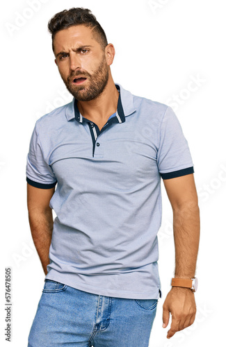 Handsome man with beard wearing casual clothes in shock face, looking skeptical and sarcastic, surprised with open mouth