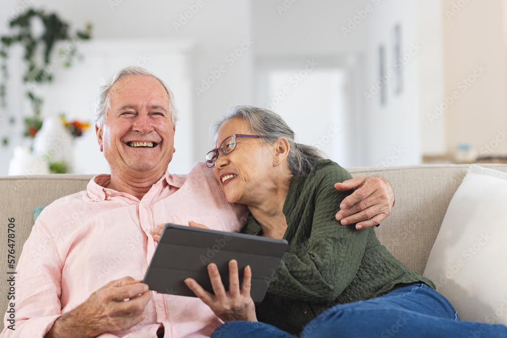 Happy senior diverse couple sitting on sofa and using tablet Happy senior diverse couple sitting on sofa and using tablet