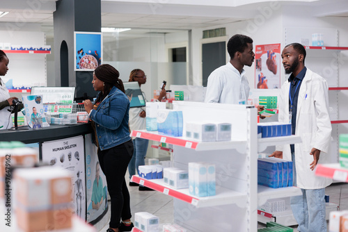 Man choosing vitamins in drugstore  woman buying prescription treatment on checkout counter. African american customers purchasing medicaments in pharmacy store  pharmacist recommending pills