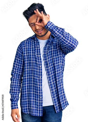 Handsome latin american young man wearing casual shirt smiling happy doing ok sign with hand on eye looking through fingers