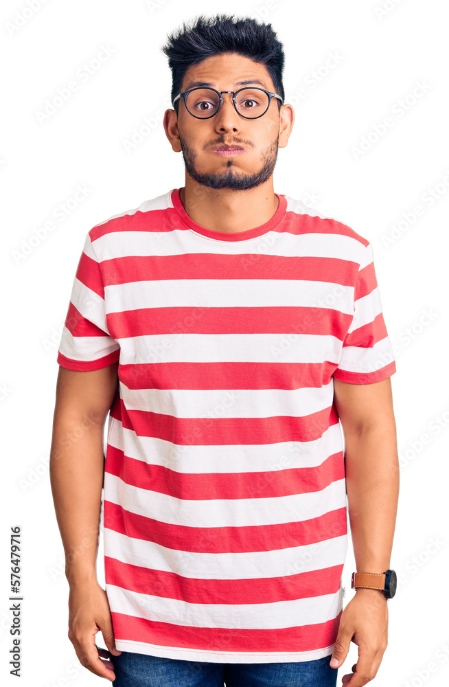 Handsome latin american young man wearing casual clothes and glasses puffing cheeks with funny face. mouth inflated with air, crazy expression. Handsome latin american young man wearing casual clothes and glasses puffing cheeks with funny face. mouth inflated with air, crazy expression.