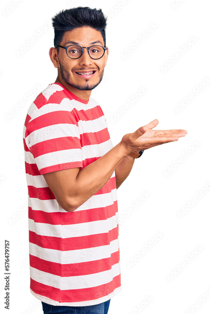 Handsome latin american young man wearing casual clothes and glasses pointing aside with hands open palms showing copy space, presenting advertisement smiling excited happy Handsome latin american young man wearing casual clothes and glasses pointing aside with hands open palms showing copy space, presenting advertisement smiling excited happy