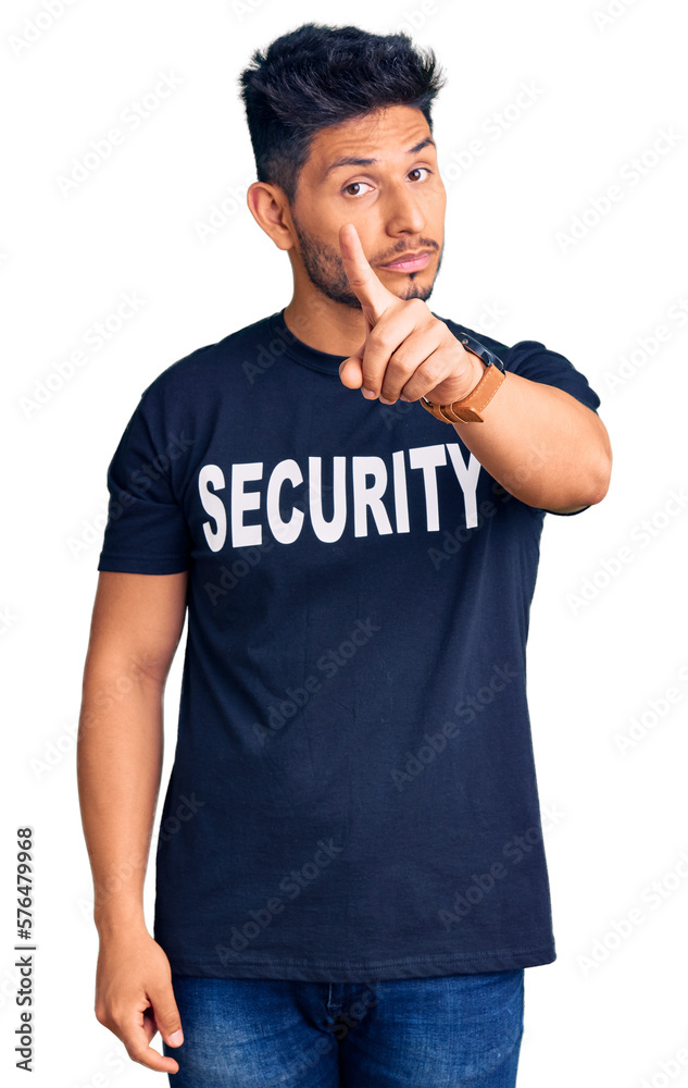 Handsome latin american young man wearing security t shirt pointing with finger up and angry expression, showing no gesture Handsome latin american young man wearing security t shirt pointing with finger up and angry expression, showing no gesture