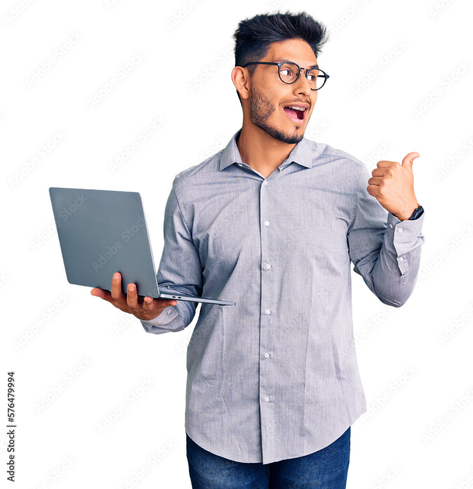 Handsome latin american young man working using computer laptop pointing thumb up to the side smiling happy with open mouth Handsome latin american young man working using computer laptop pointing thumb up to the side smiling happy with open mouth