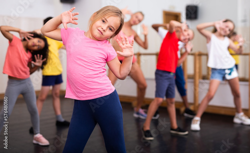 Portrait of cheerful preteen girl practicing dance movements with group of children in choreography class