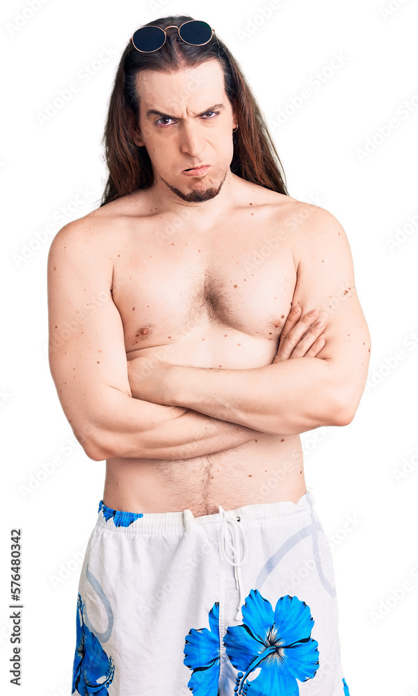 Fototapeta premium Young adult man with long hair wearing swimwear shirtless skeptic and nervous, disapproving expression on face with crossed arms. negative person.
