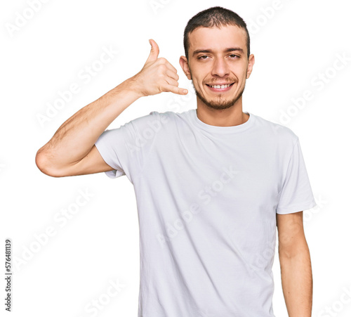 Hispanic young man wearing casual white t shirt smiling doing phone gesture with hand and fingers like talking on the telephone. communicating concepts.