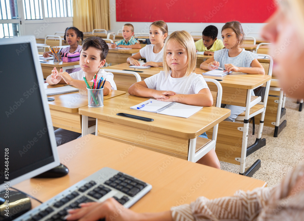 Fototapeta premium Portrait of diligent towheaded preteen girl looking at camera during lesson in primary school