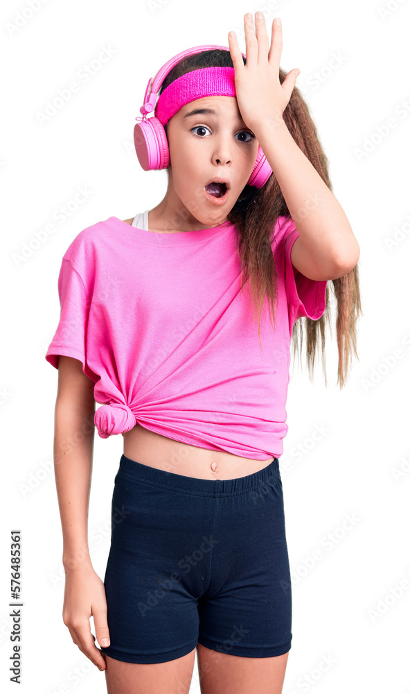 Cute hispanic child girl wearing gym clothes and using headphones surprised with hand on head for mistake, remember error. forgot, bad memory concept. Cute hispanic child girl wearing gym clothes and using headphones surprised with hand on head for mistake, remember error. forgot, bad memory concept.