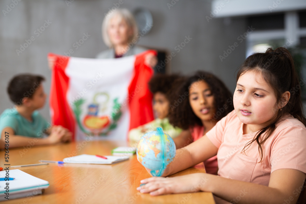 Fototapeta premium Concentrated ten-year-old schoolgirl studying the history of Peru in lesson and attentively looking for her on the globe