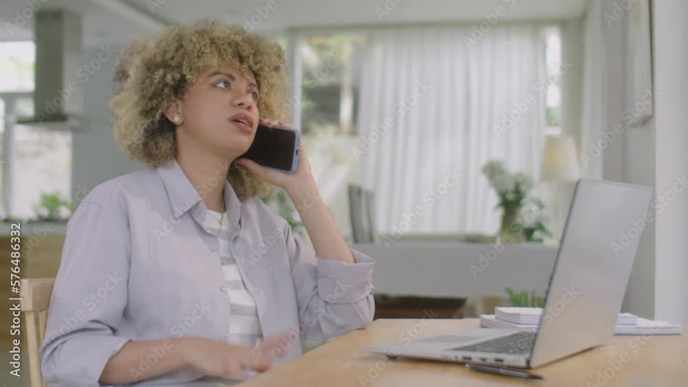 Medium shot of young Latin woman sitting at desk with laptop and speaking on mobile phone while working in home office Medium shot of young Latin woman sitting at desk with laptop and speaking on mobile phone while working in home office