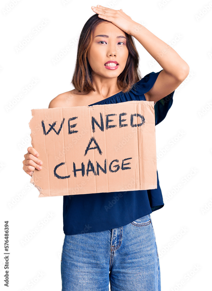 Young beautiful chinese girl holding we need a change banner stressed and frustrated with hand on head, surprised and angry face Young beautiful chinese girl holding we need a change banner stressed and frustrated with hand on head, surprised and angry face