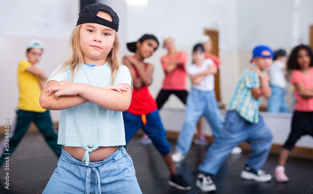 Portrait of cheerful preteen girl practicing dance movements with group of children in choreography class