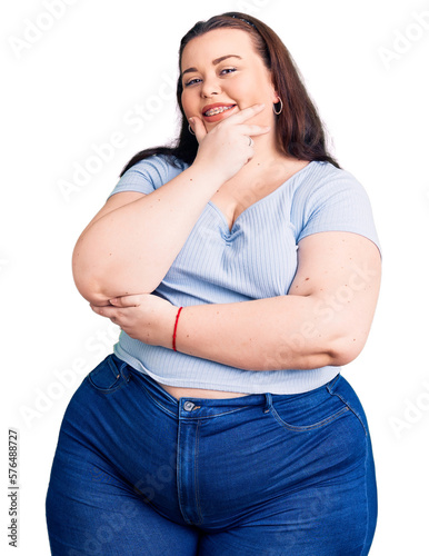 Young plus size woman wearing casual clothes looking confident at the camera smiling with crossed arms and hand raised on chin. thinking positive.