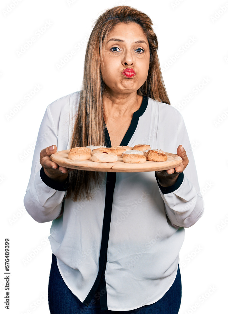 Middle age latin woman eating pastries puffing cheeks with funny face. mouth inflated with air, catching air. Middle age latin woman eating pastries puffing cheeks with funny face. mouth inflated with air, catching air.