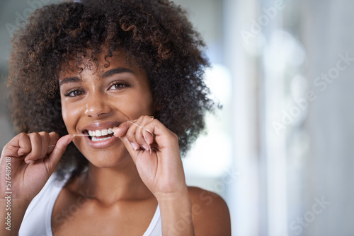 Getting those hard to reach places. Shot of a young woman flossing her teeth in the mirror.