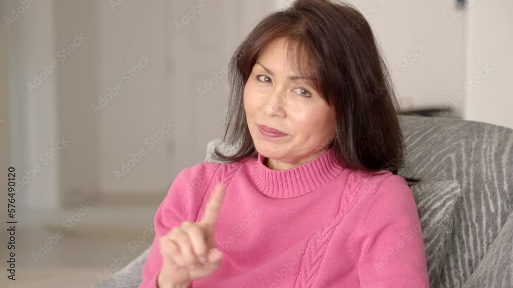 Beautiful stylish woman in pink sweater looking at camera enjoying smiling making three humorous hand gestures: do not do something, I do not know and be quiet sitting in living room chair. Beautiful stylish woman in pink sweater looking at camera enjoying smiling making three humorous hand gestures: do not do something, I do not know and be quiet sitting in living room chair.