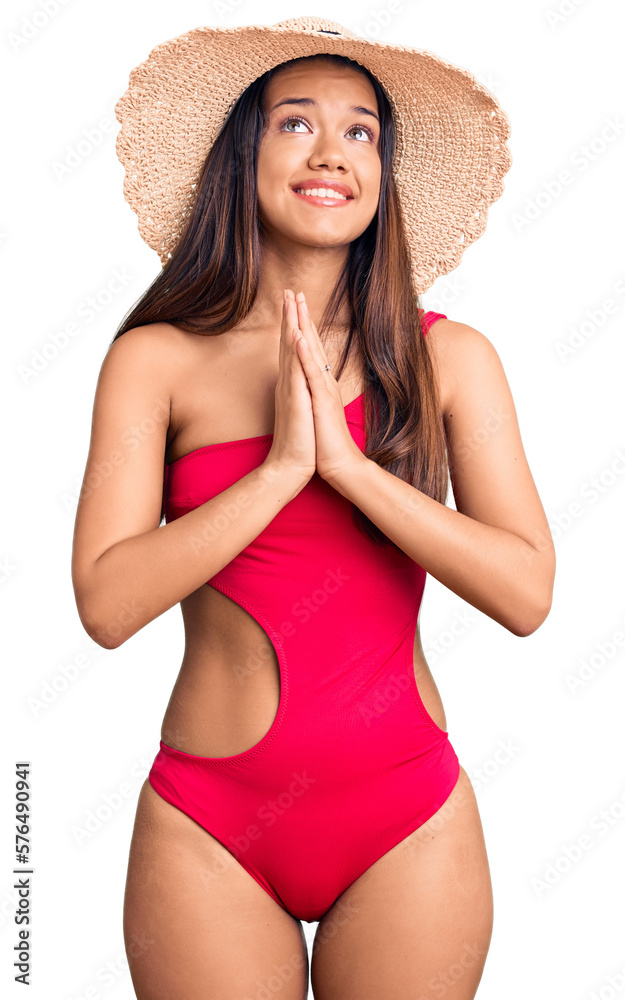 Young beautiful latin girl wearing swimwear and summer hat begging and praying with hands together with hope expression on face very emotional and worried. begging. Young beautiful latin girl wearing swimwear and summer hat begging and praying with hands together with hope expression on face very emotional and worried. begging.
