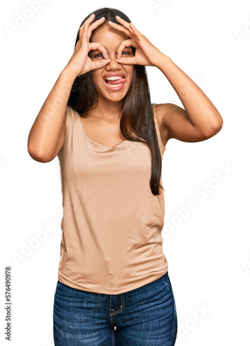 Beautiful hispanic woman wearing casual clothes doing ok gesture like binoculars sticking tongue out, eyes looking through fingers. crazy expression. © Krakenimages.com