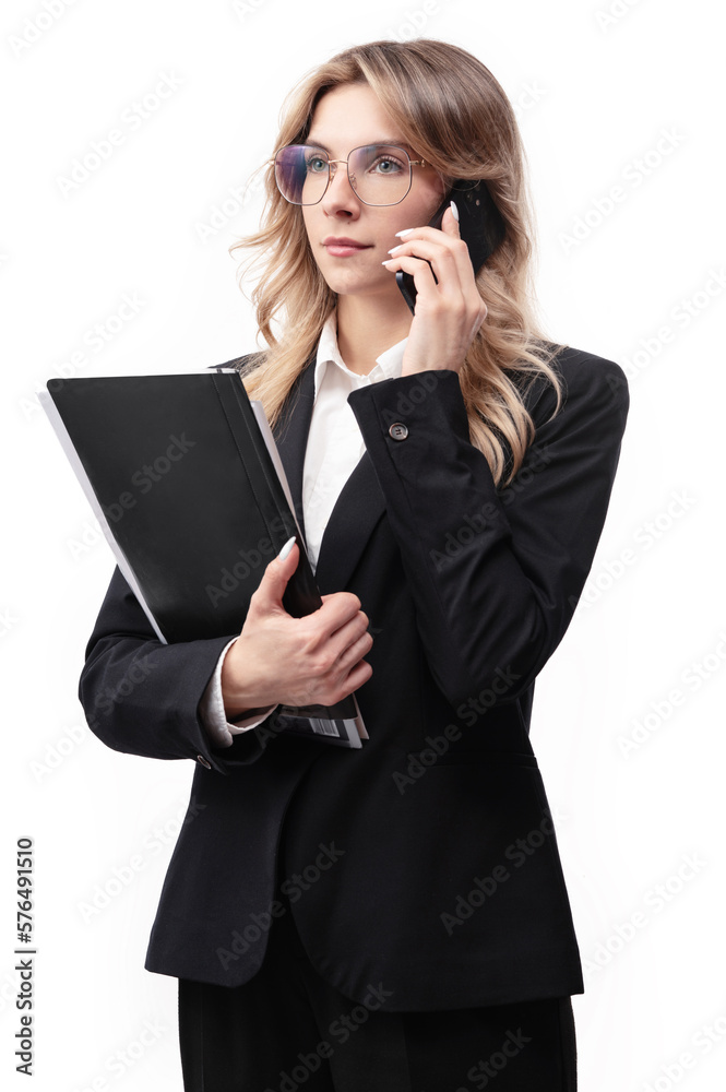 Young business woman or office worker wearing a black suit holding documents and talking on the phone. Smiling business woman isolated on white background.
Young business woman or office worker wearing a black suit holding documents and talking on the phone. Smiling business woman isolated on white background.