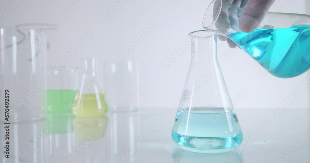 Scientist chemist pouring blue liquid into beaker
Scientist chemist pouring blue liquid into beaker