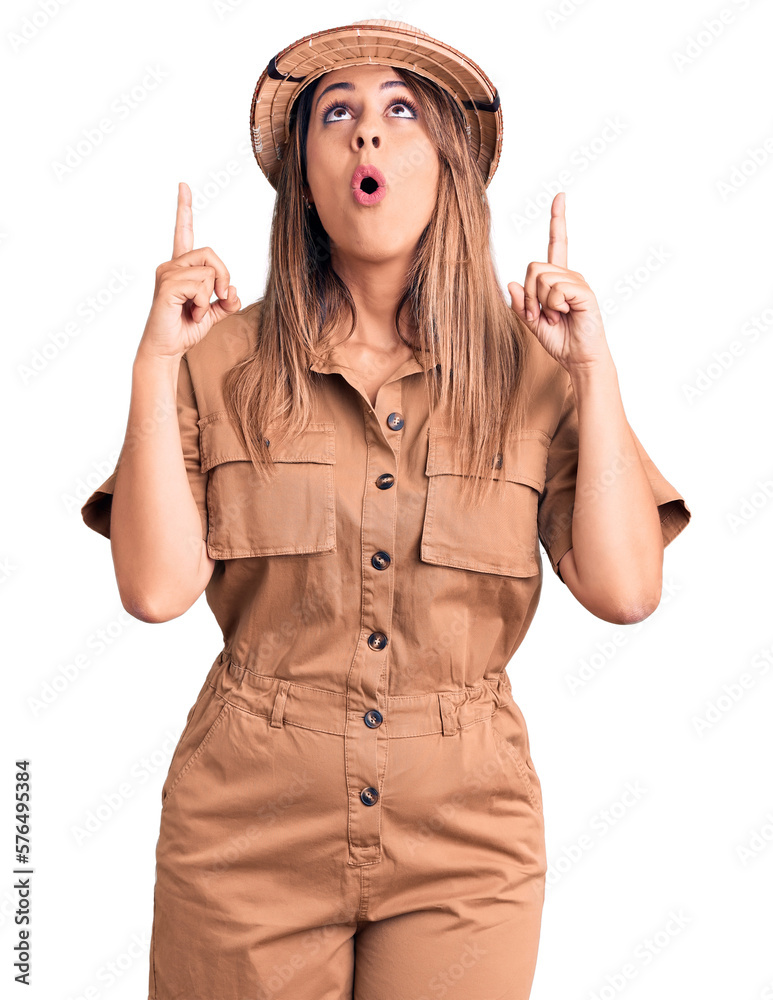 Young beautiful woman wearing explorer hat amazed and surprised looking up and pointing with fingers and raised arms. Young beautiful woman wearing explorer hat amazed and surprised looking up and pointing with fingers and raised arms.