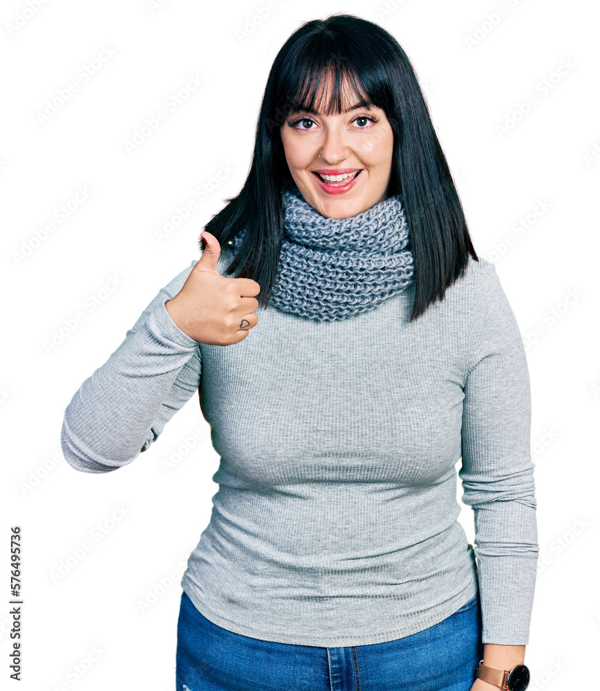 Young hispanic plus size woman wearing winter scarf doing happy thumbs up gesture with hand. approving expression looking at the camera showing success. Young hispanic plus size woman wearing winter scarf doing happy thumbs up gesture with hand. approving expression looking at the camera showing success.