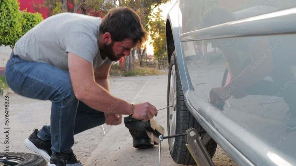 young traveling man changing a flat tire on the roadside, using a hazard triangle