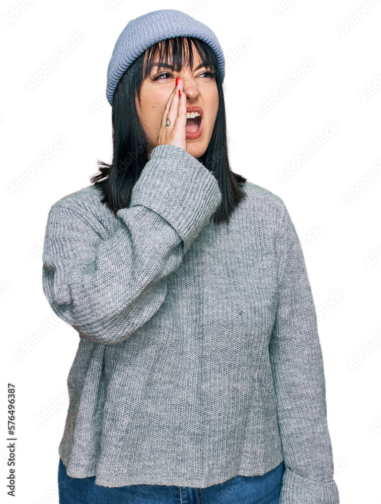 Young hispanic woman wearing cute wool cap shouting and screaming loud to side with hand on mouth. communication concept. Young hispanic woman wearing cute wool cap shouting and screaming loud to side with hand on mouth. communication concept.