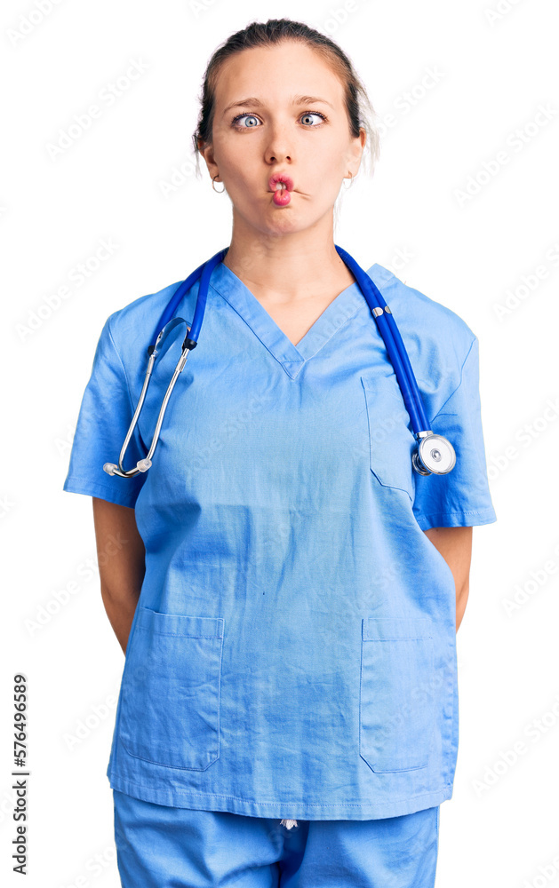 Young beautiful blonde woman wearing doctor uniform and stethoscope making fish face with lips, crazy and comical gesture. funny expression.