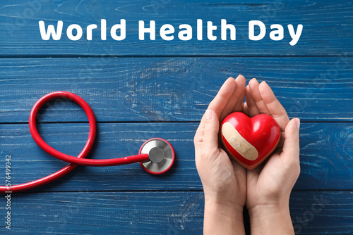 Hands holding red heart and stethoscope on wooden background. World Health Day photo