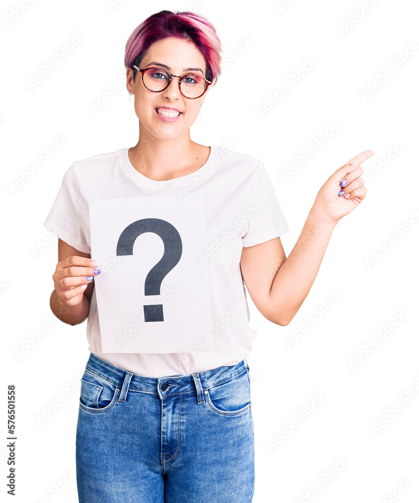 Young beautiful woman with pink hair holding question mark smiling happy pointing with hand and finger to the side Young beautiful woman with pink hair holding question mark smiling happy pointing with hand and finger to the side