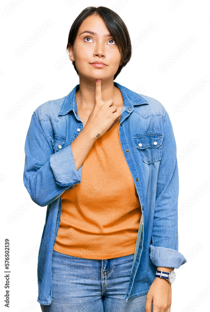 Young beautiful hispanic woman with short hair wearing casual denim jacket thinking concentrated about doubt with finger on chin and looking up wondering