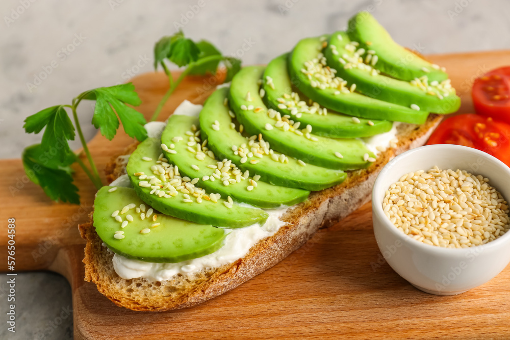 Board with delicious avocado toast and sesame seeds on grey background Board with delicious avocado toast and sesame seeds on grey background
