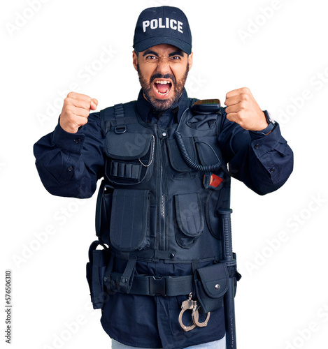 Young hispanic man wearing police uniform angry and mad raising fists frustrated and furious while shouting with anger. rage and aggressive concept.