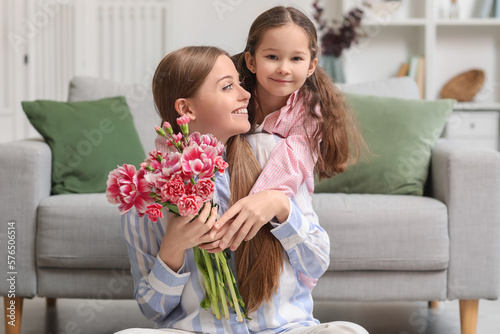 Cute little girl hugging her mother with flowers at home on holiday