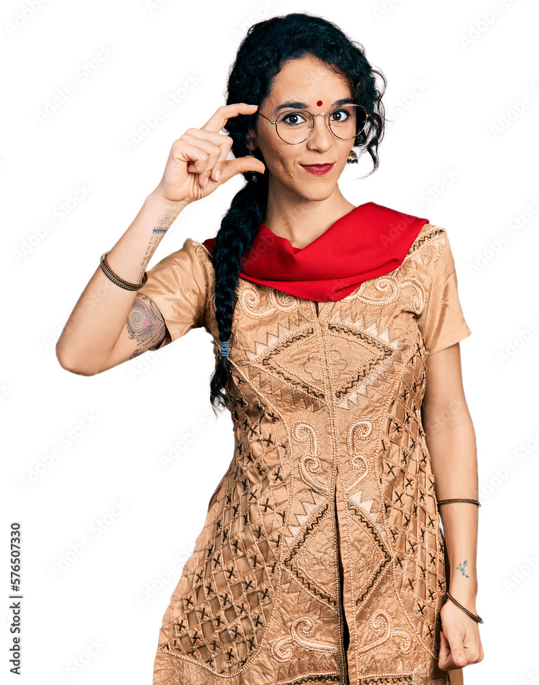 Young indian woman wearing traditional dress and glasses smiling and confident gesturing with hand doing small size sign with fingers looking and the camera. measure concept. Young indian woman wearing traditional dress and glasses smiling and confident gesturing with hand doing small size sign with fingers looking and the camera. measure concept.