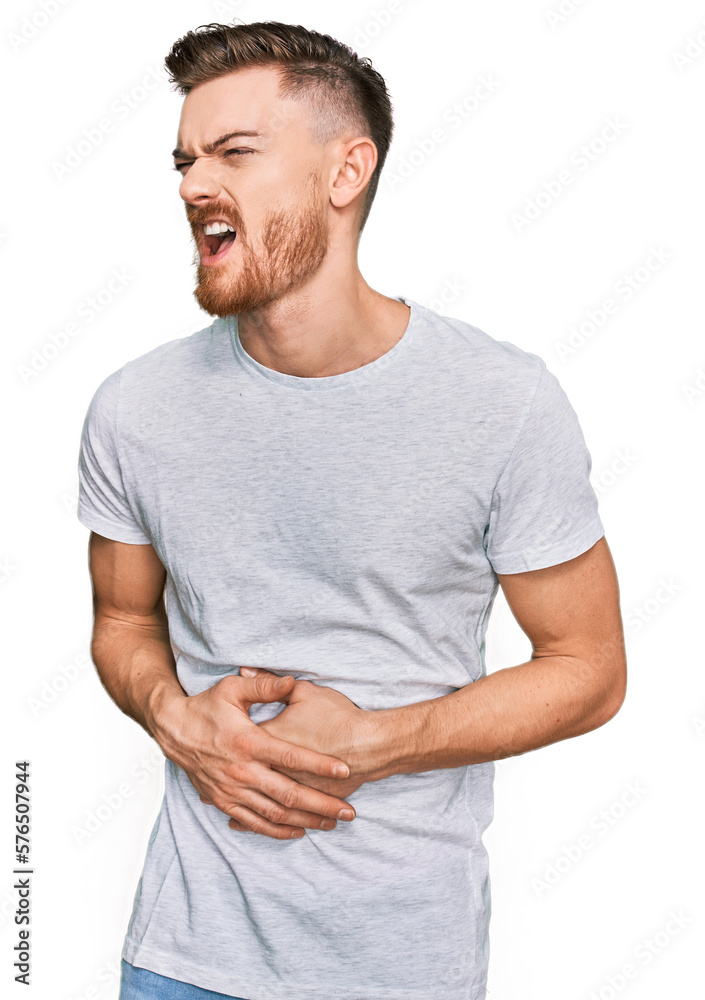 Young redhead man wearing casual grey t shirt with hand on stomach because nausea, painful disease feeling unwell. ache concept. Young redhead man wearing casual grey t shirt with hand on stomach because nausea, painful disease feeling unwell. ache concept.