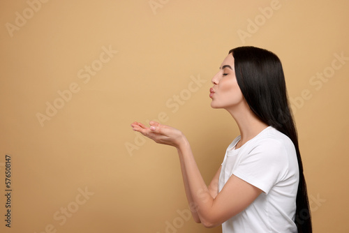 Beautiful young woman blowing kiss on beige background. Space for text