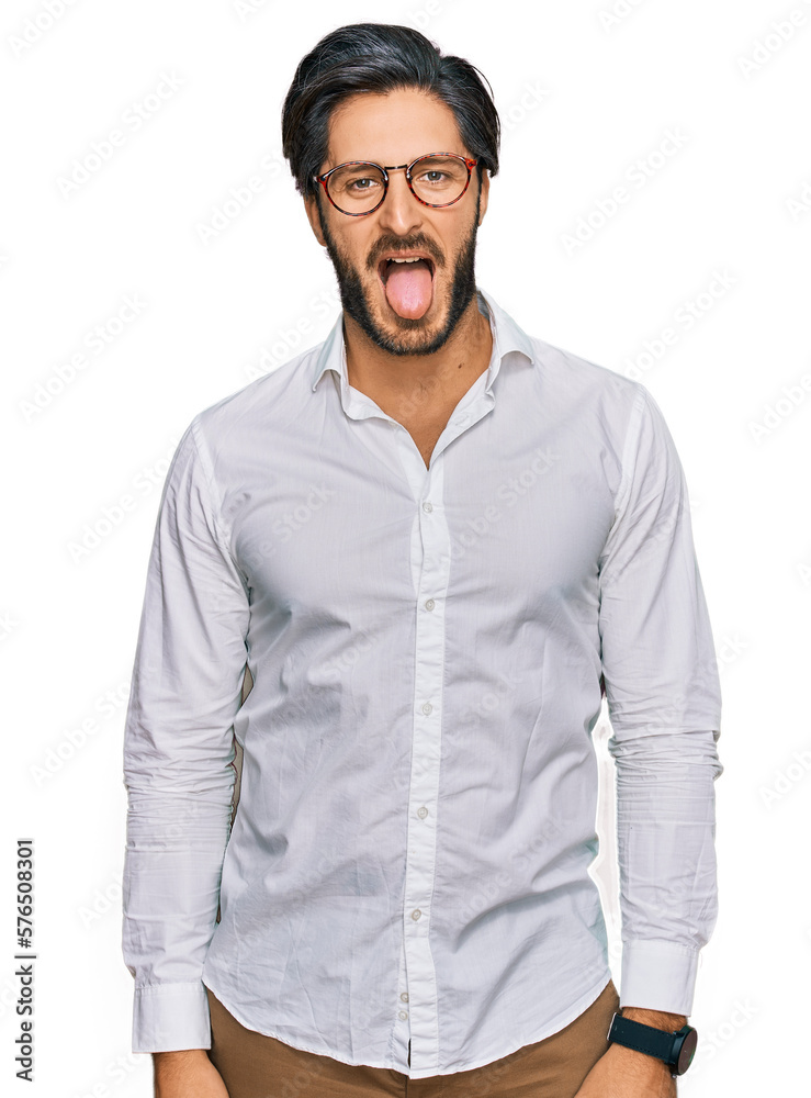 Young hispanic man wearing business shirt and glasses sticking tongue out happy with funny expression. emotion concept. Young hispanic man wearing business shirt and glasses sticking tongue out happy with funny expression. emotion concept.