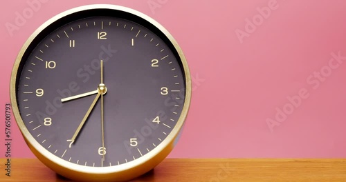 4K footage Time-lapse, black desk clock inlaid with gold frame is placed on the wooden floor with a pink background, walk and tell at 8 o'clock in the morning It takes 1 hour. photo