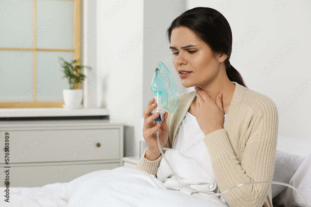 Sick young woman using nebulizer on bed at home, space for text Sick young woman using nebulizer on bed at home, space for text