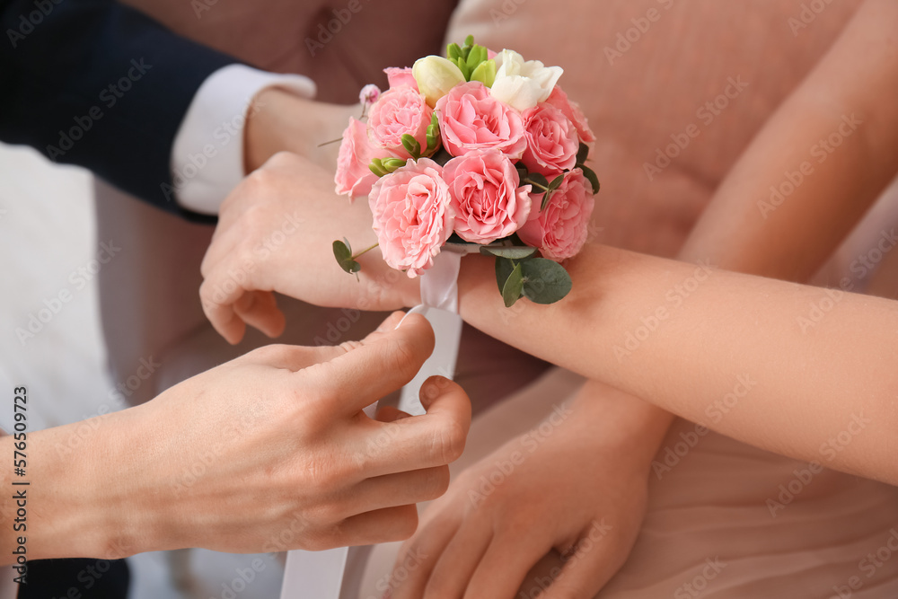 Teenage boy tying corsage around his girlfriend's wrist for prom in room, closeup Teenage boy tying corsage around his girlfriend's wrist for prom in room, closeup