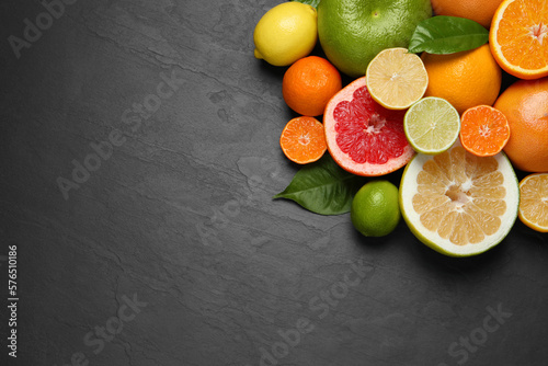 Different ripe citrus fruits with green leaves on black table, flat lay. Space for text © New Africa