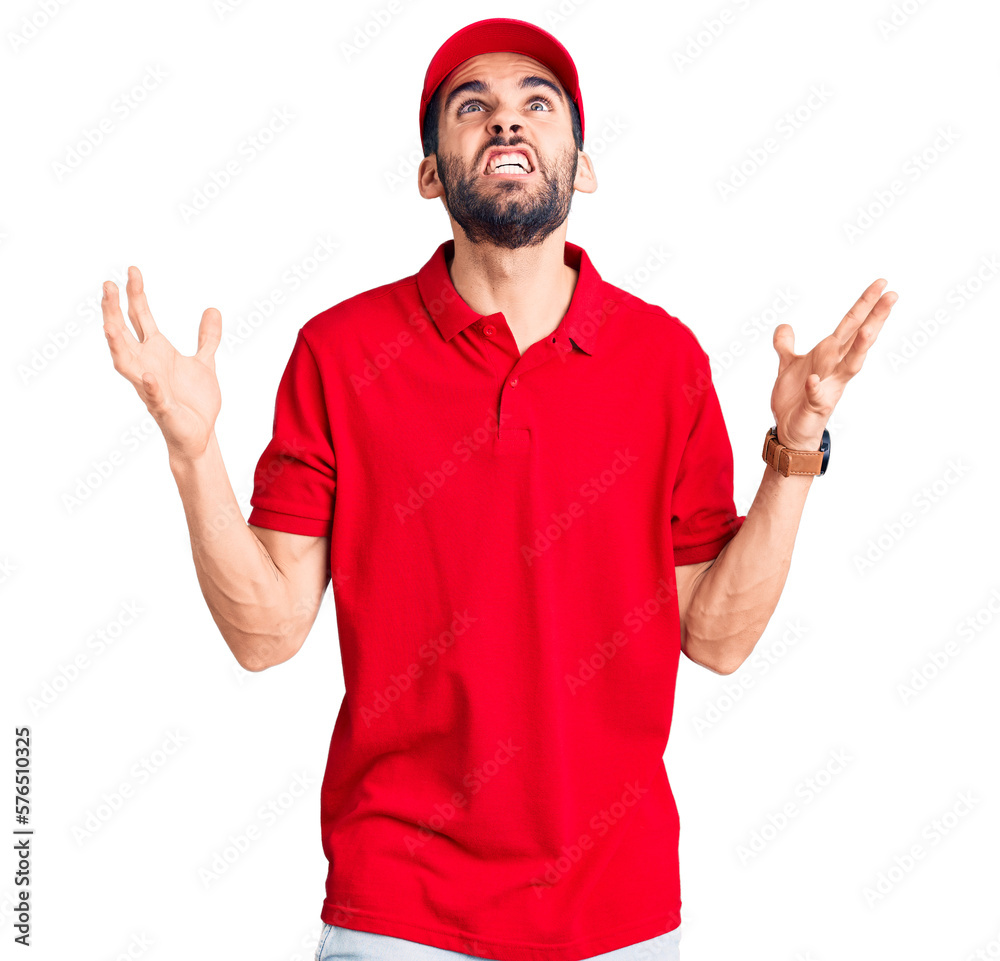 Naklejka premium Young handsome man with beard wearing delivery uniform crazy and mad shouting and yelling with aggressive expression and arms raised. frustration concept.
