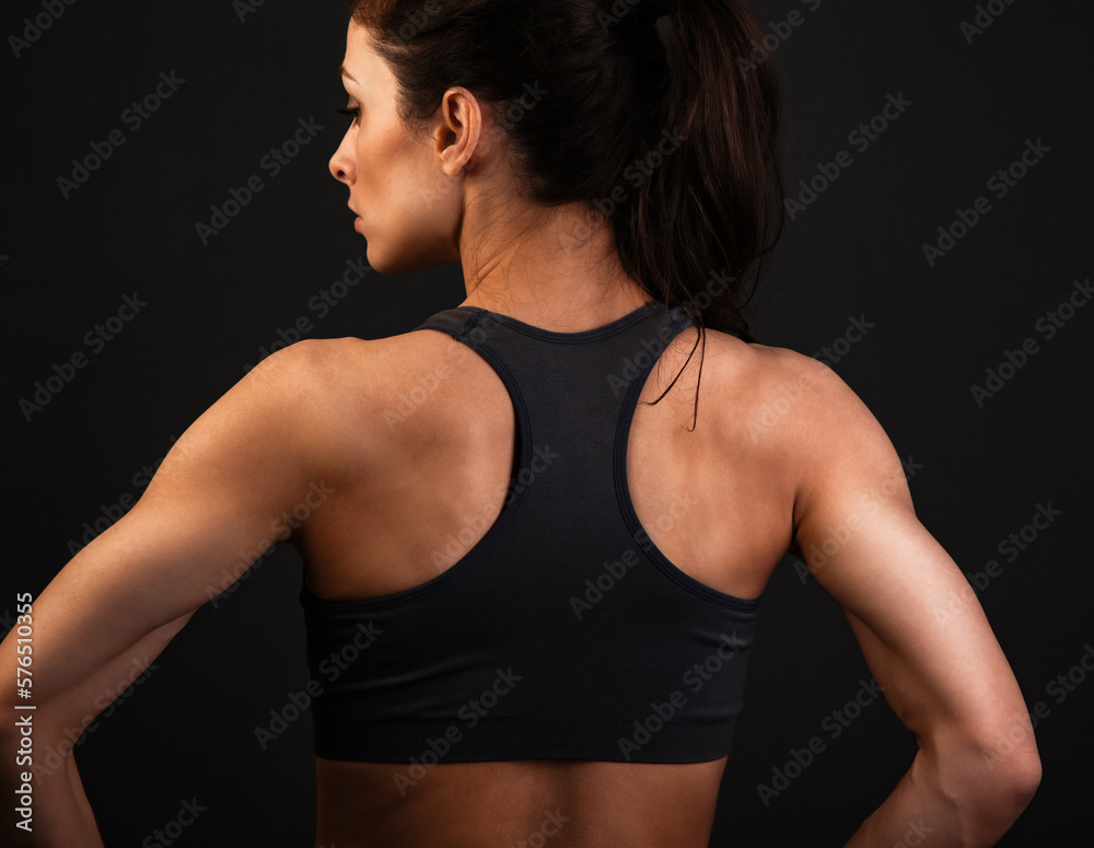 Sporty strong woman body standing in sport clothing bra. Back view. Studio healthy life style portrait in art dark shadows. Sporty strong woman body standing in sport clothing bra. Back view. Studio healthy life style portrait in art dark shadows.