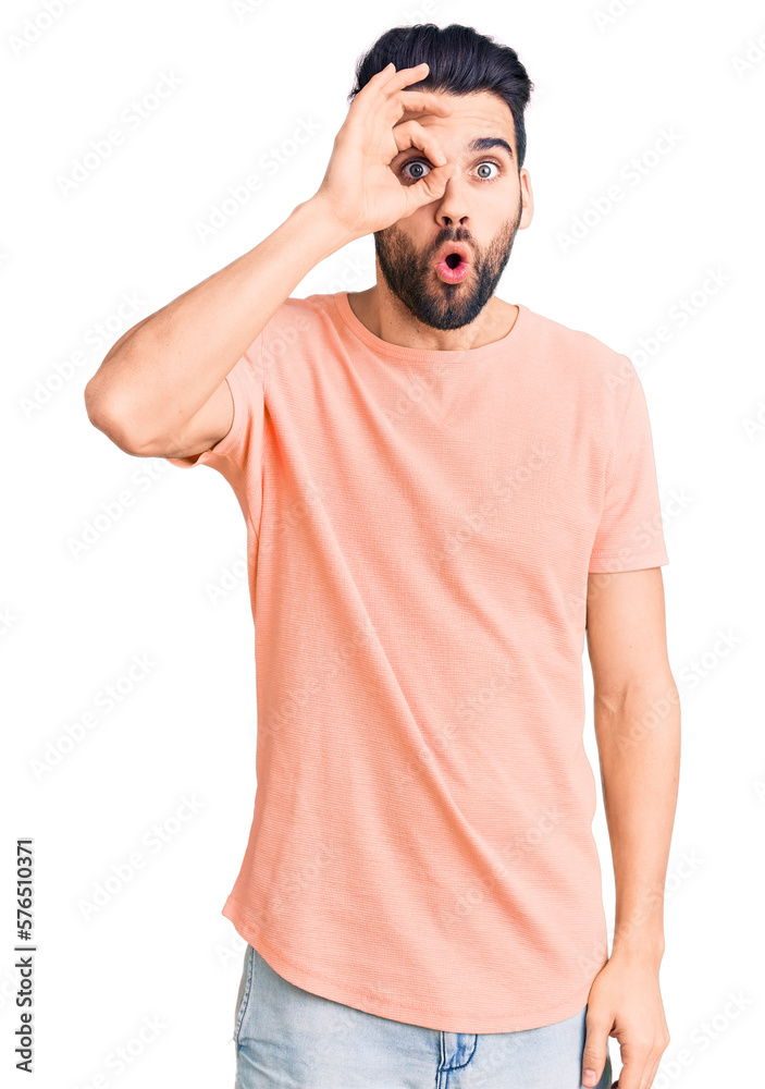Young handsome man with beard wearing casual t-shirt doing ok gesture shocked with surprised face, eye looking through fingers. unbelieving expression. Young handsome man with beard wearing casual t-shirt doing ok gesture shocked with surprised face, eye looking through fingers. unbelieving expression.
