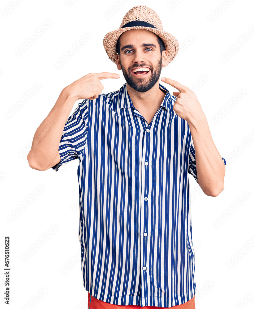 Naklejka premium Young handsome man with beard wearing summer hat and striped shirt smiling cheerful showing and pointing with fingers teeth and mouth. dental health concept.